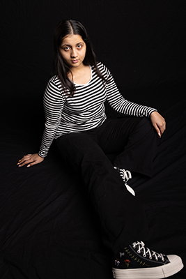 Riddhi with black and white striped top, sitting, full body photo.