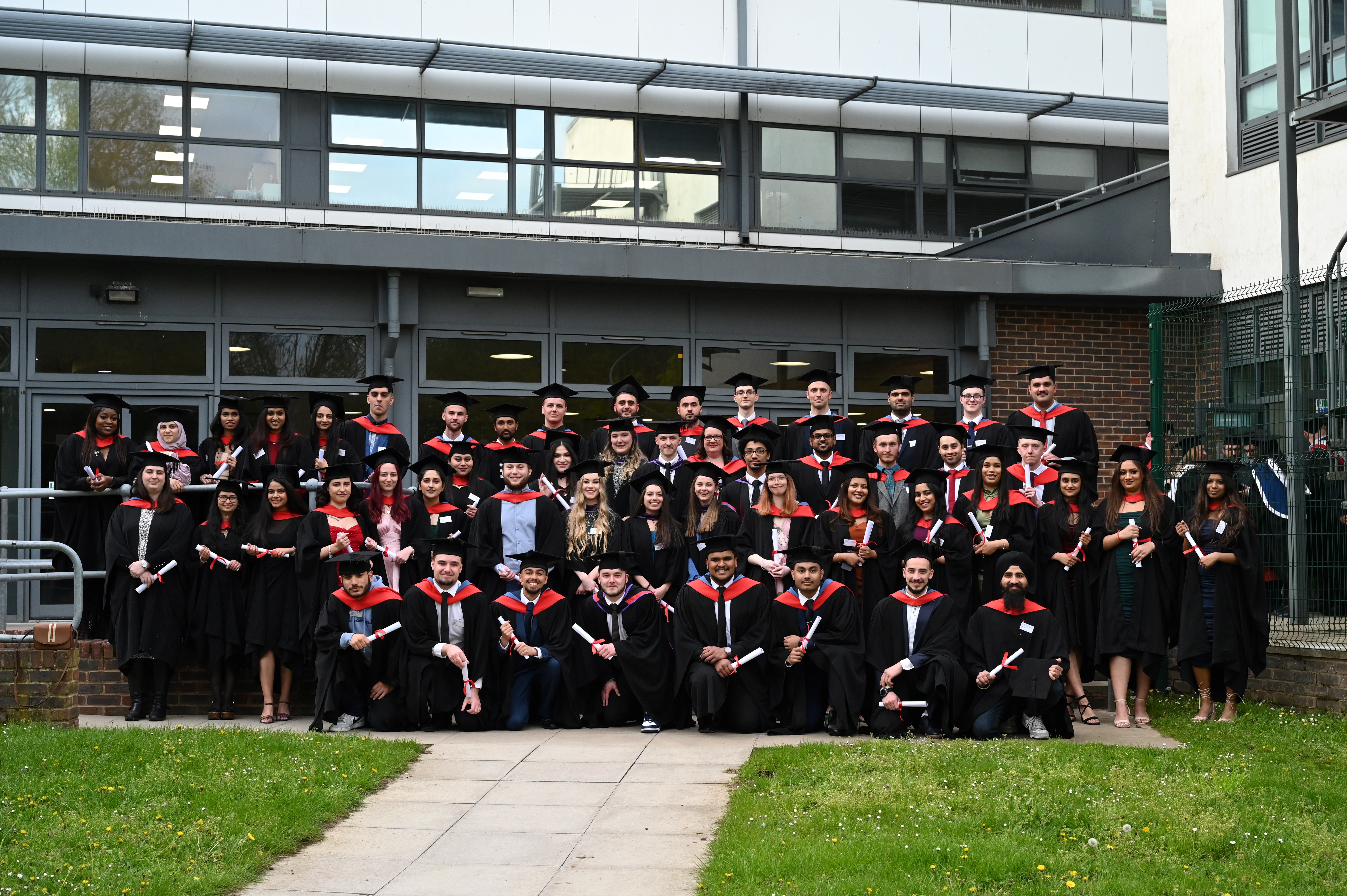 Formal group of Uxbridge College and Harrow College graduates outside Uxbridge College building at their HE Graduation
