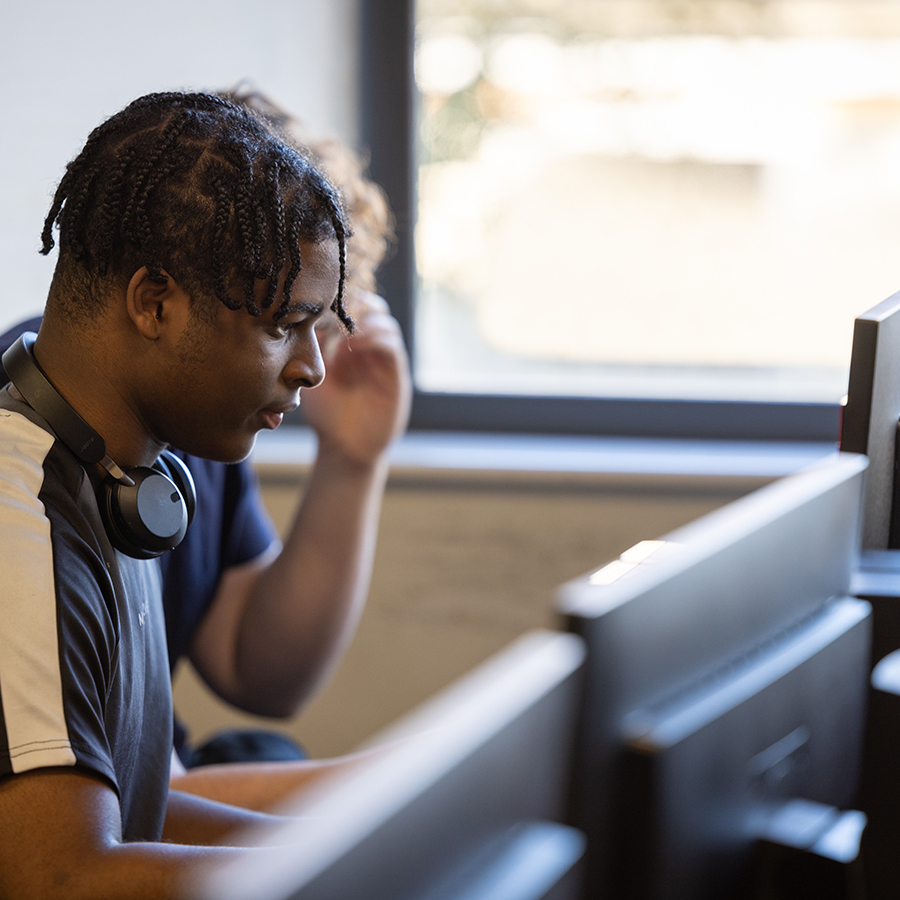 A male Uxbridge student working on the computer with headphones around his neck